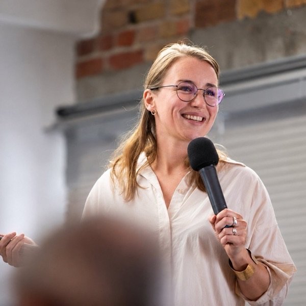 Lia Weitz moderiert mit Mikrofon vor einer Gruppe